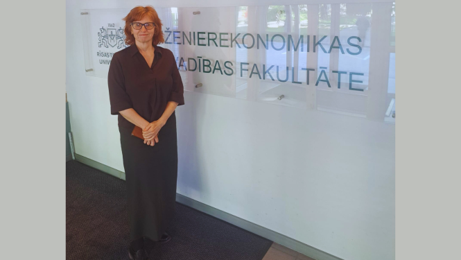 Fotogrāfijā redzama Baiba Vītoliņa, Būvniecības valsts kontroles biroja direktore. Viņa stāv ar saliktām rokām un klusu smaidu Rīgas Tehniskās universitātes telpās, blakus stikla sienai ar uzrakstu latviešu valodā "INŽENIEREKONOMIKAS UN VADĪBAS FAKULTĀTE".