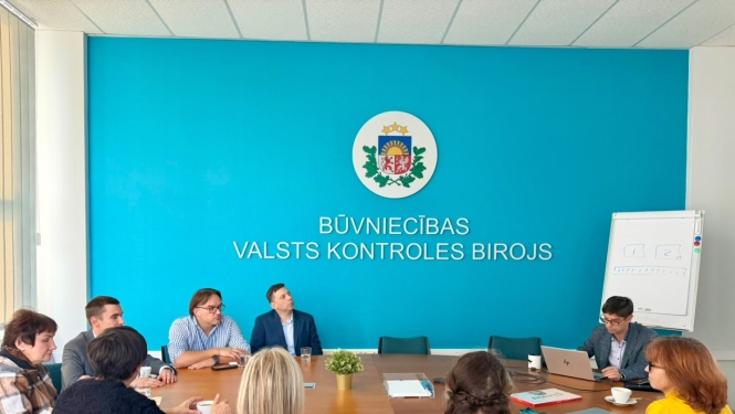 Veselības inspekcijas un Būvniecības valsts kontroles biroja pārstāvju tikšanās BVKB telpās. Dalībnieki sēž pie sanāksmju galda un klausās prezentāciju par Būvniecības informācijas sistēmas darbību.