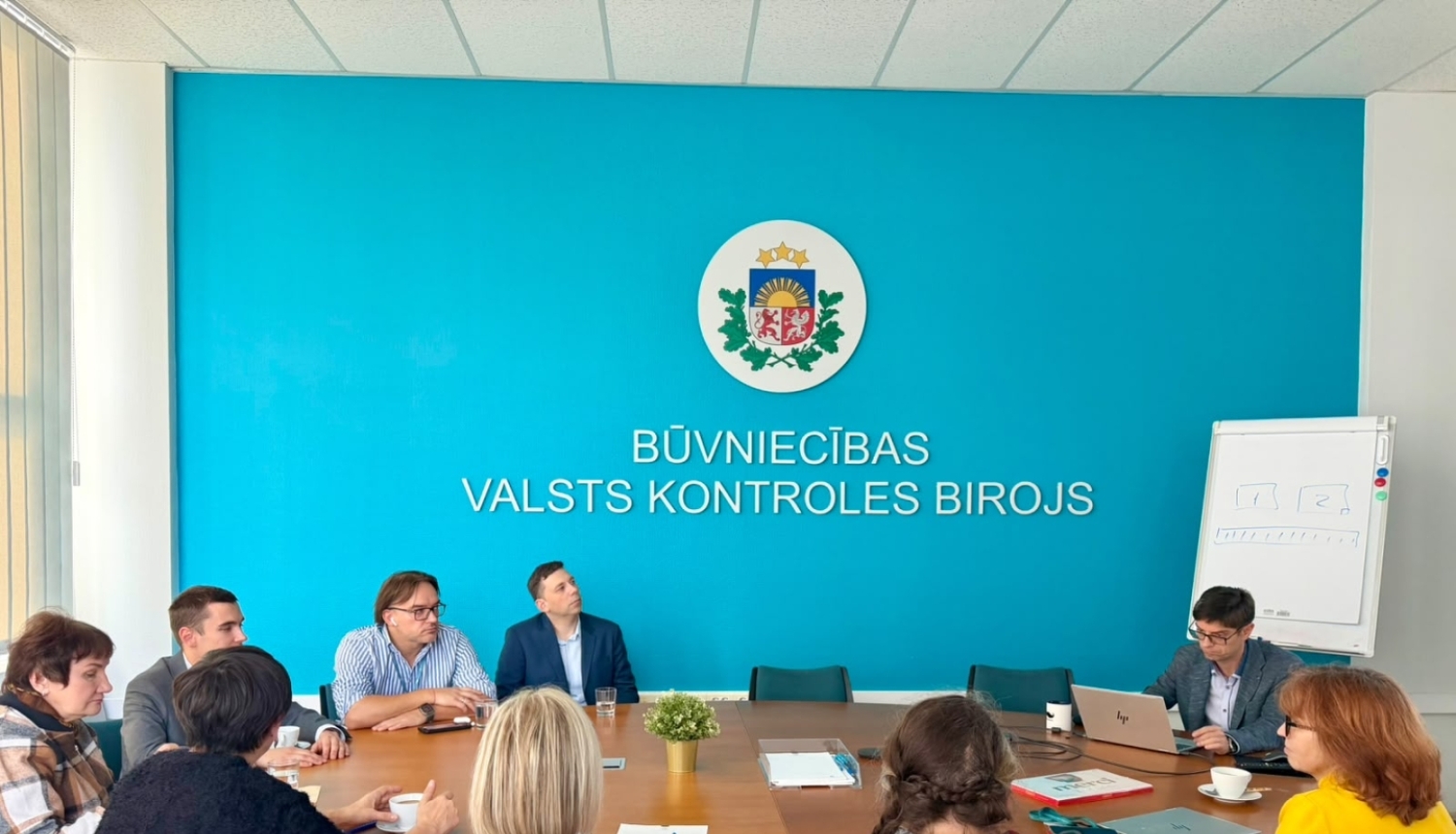 Veselības inspekcijas un Būvniecības valsts kontroles biroja pārstāvju tikšanās BVKB telpās. Dalībnieki sēž pie sanāksmju galda un klausās prezentāciju par Būvniecības informācijas sistēmas darbību.