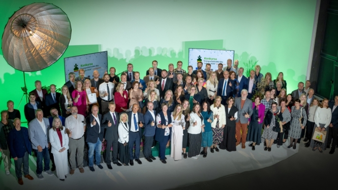 Kopbilde no konkursa “Energoefektīvākā ēka Latvijā 2026” apbalvošanas pasākuma. Uz skatuves kopā fotografējas konkursa dalībnieki, laureāti un organizatoru pārstāvji; fonā redzami konkursa vizuālie materiāli.