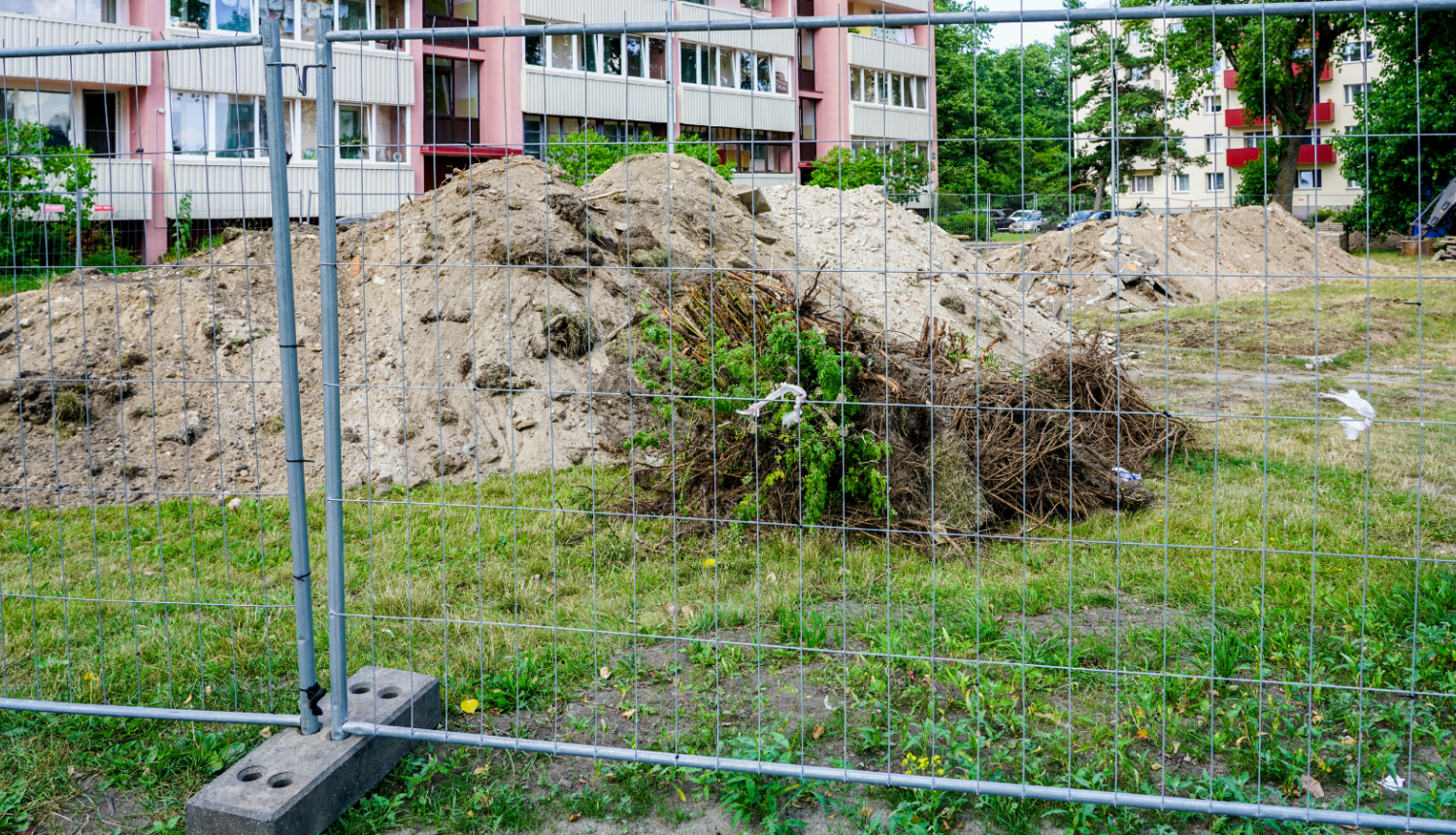 Attēlā žogs, aiz kura atrodas grants kaudzes dzīvojamā nama pagalmā